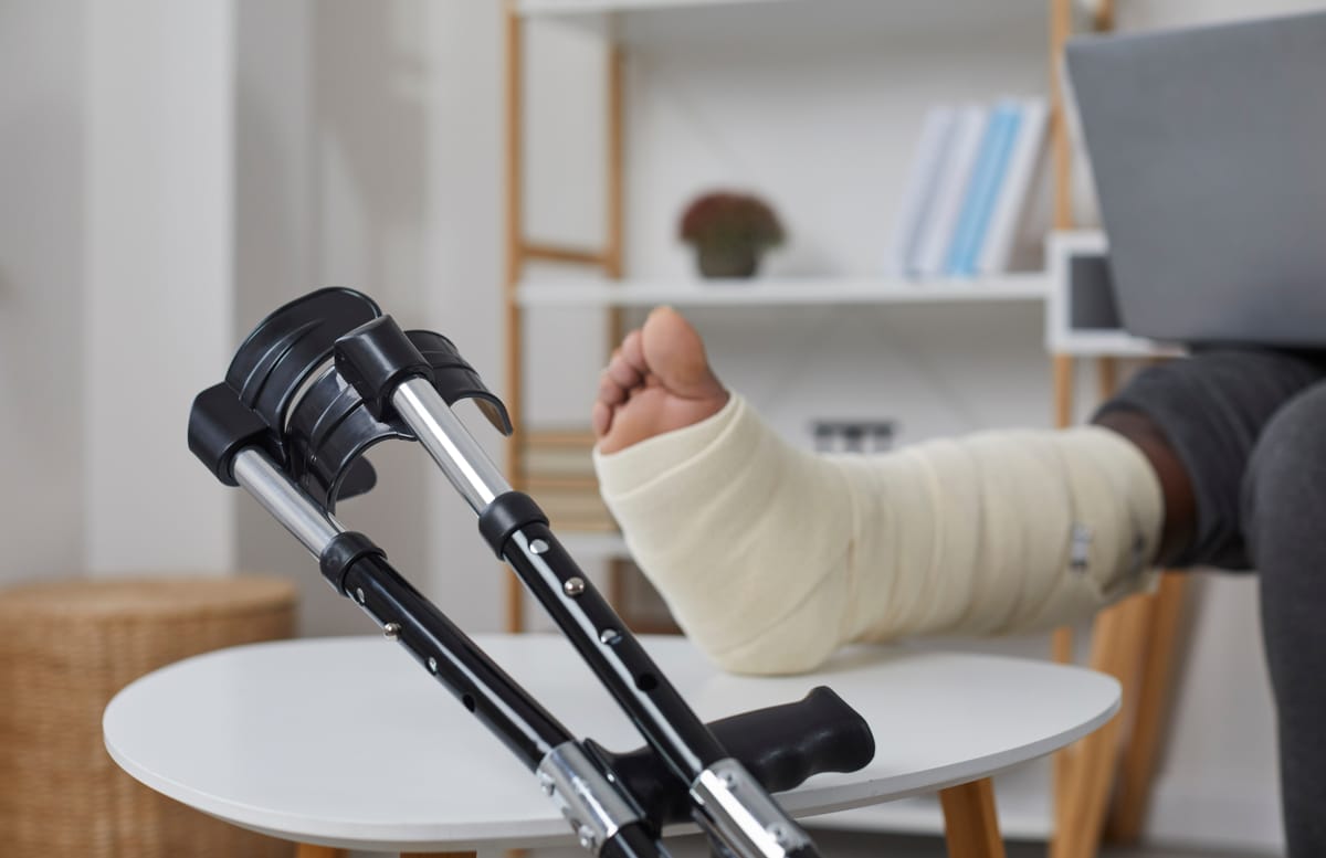 Person mit Gipsbein und Gehhilfen wird zu Hause betreut