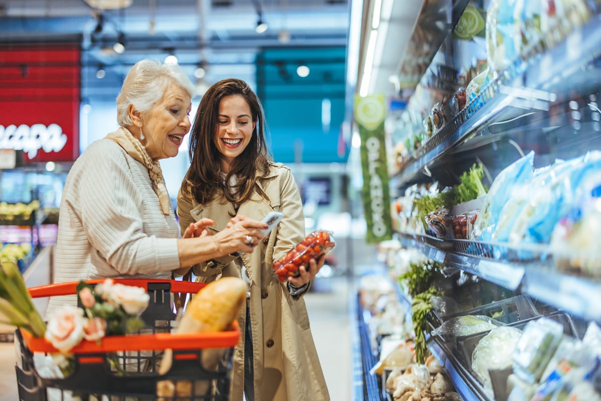 Einkaufshilfe begleitet Seniorin beim Einkauf im Supermarkt