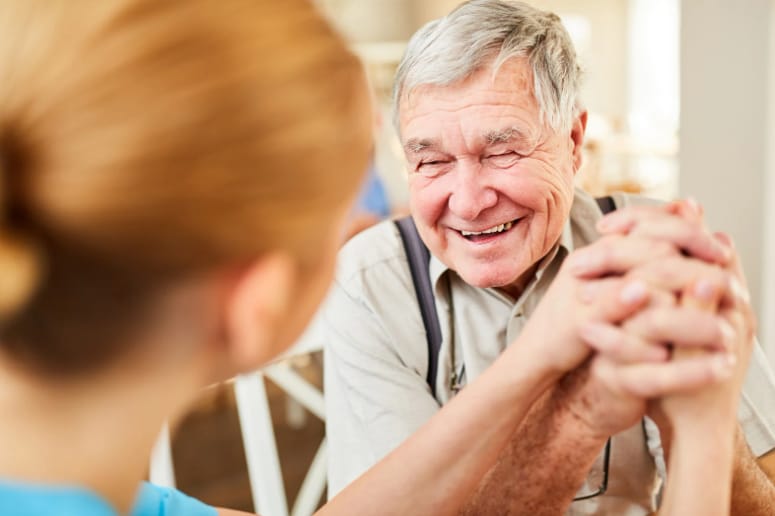 Lächelnder Senior hält dankbar die Hände einer Betreuungskraft